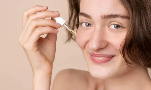 Une femme souriante applique une goutte de sérum à la vitamine C sur son visage. C'est le moment idéal pour utiliser la vitamine C sur le visage pour une peau éclatante.