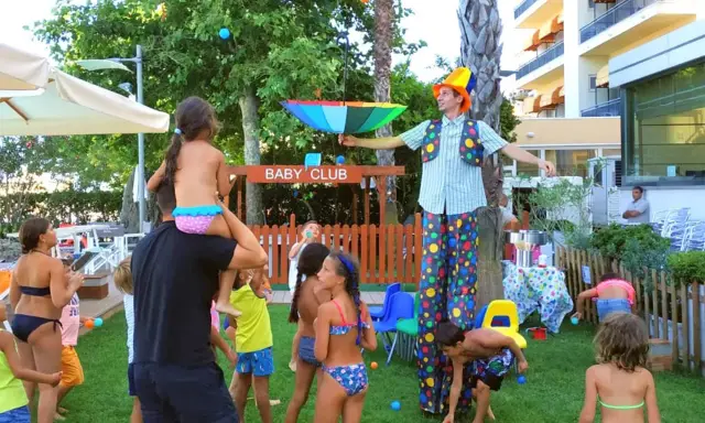 Hotel con biberoneria: animazione al Baby Club con un clown che intrattiene i bambini con palline colorate e un ombrello arcobaleno.