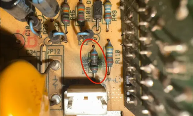 Uszkodzony opornik z czerwonym okręgiem na płytce drukowanej, obok innych elementów elektronicznych.
