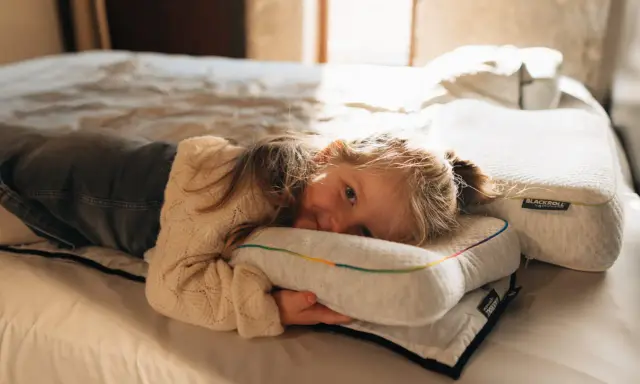 Ein kleines Mädchen kuschelt sich auf einem Bett an ein Kissen. Die Schlafphasen von Kindern sind wichtig für ihre Entwicklung.