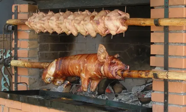 Ein Spanferkel grillen über offenem Feuer. Darüber hängen mehrere Hähnchen am Spieß.