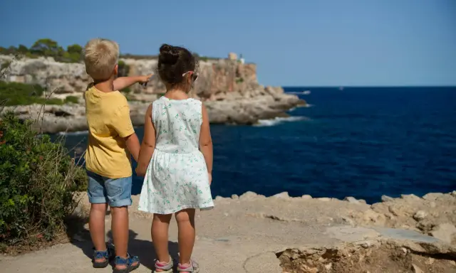 Två barn står vid havet, redo för sommarlåtar och skolavslutning. Pojken pekar mot horisonten.