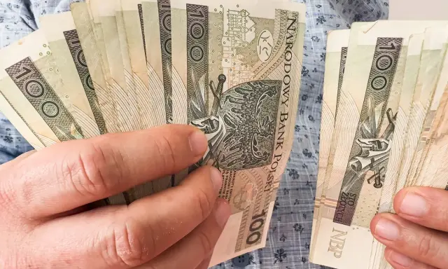 Ręce trzymające plik banknotów 100 zł. Planowanie finansowe, jak wybrać najkorzystniejsze lata do emerytury, wymaga analizy oszczędności.