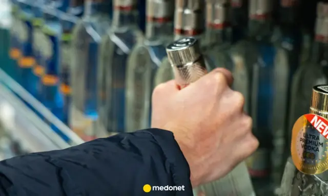Dłoń sięga po butelkę wódki, a artykuł na medonet.pl analizuje wpływ alkoholu, w tym piwa, na białe krwinki.