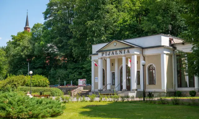 Duszniki Zdrój atrakcje: Pijalnia wód mineralnych z kolumnadą i wieżą kościelną w tle.