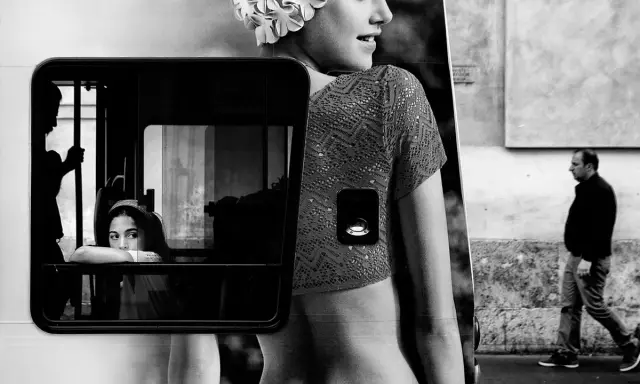 Un'istantanea di vita urbana che ricorda i fotografi di moda, con una ragazza che guarda fuori da un finestrino e un uomo che cammina sullo sfondo.