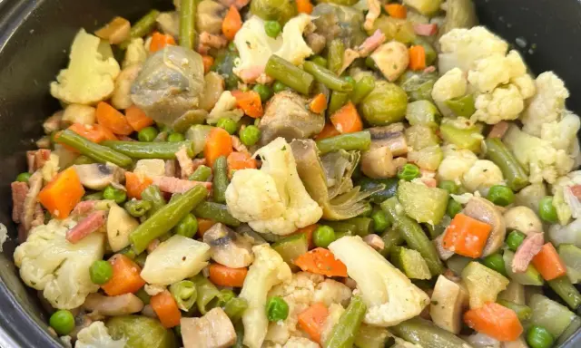 Un plato abundante de menestra de verduras, con brócoli, zanahoria, judías verdes, guisantes y trozos de tocino.