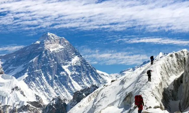 Alpinisci wspinają się na ośnieżony grzbiet, zbliżając się do jednego z najwyższych szczytów kontynentów.