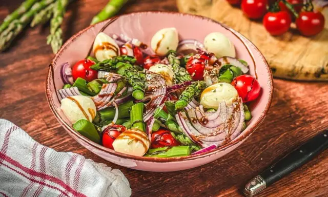 Frischer Spargelsalat mit Ei, Tomaten, roten Zwiebeln und Mozzarella-Kugeln, beträufelt mit Balsamico-Dressing.