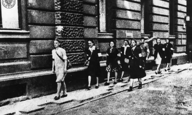 Kobiety w powstaniu warszawskim, idące ulicą. Na ramionach mają opaski.