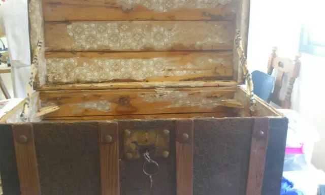 Proceso de restaurar baúl antiguo de chapa y madera. El interior muestra madera desgastada y papel tapiz despegado.