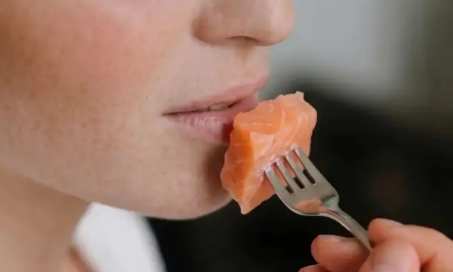 Une personne mange un morceau de saumon à la fourchette. Un aperçu de son visage, idéal pour un avis sur le régime Natman.