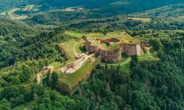 Forteca na zielonym wzgórzu, niczym srebrna góra otoczona lasem, wita zwiedzających.