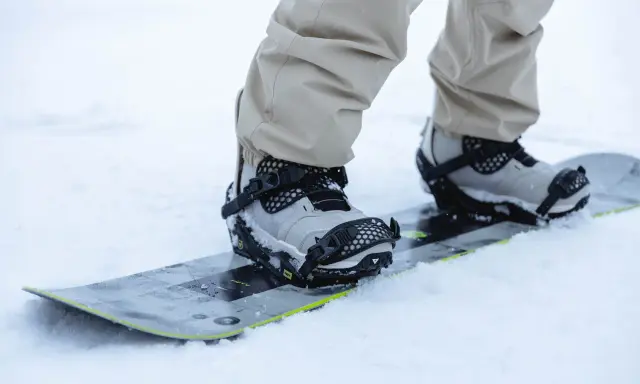 Snowboarder w beżowych spodniach zapina wiązania snowboardowe szybkie zapinanie. Gotowy na jazdę po śniegu.
