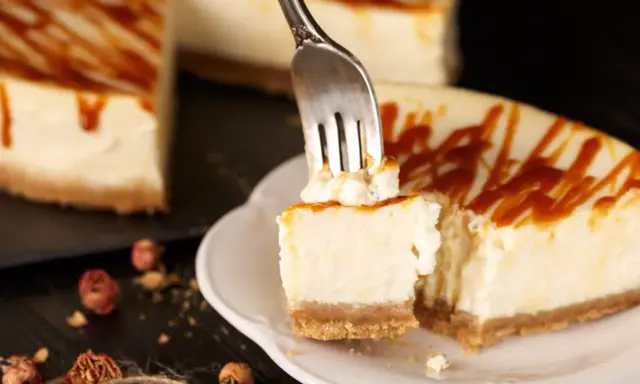 Une fourchette prélève un morceau crémeux de cheesecake, révélant le fromage frais onctueux sous un filet de caramel.