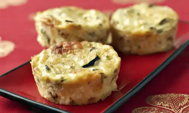 Trois petits flans de courgettes dorés et appétissants sur une assiette rouge, parfaits pour un repas léger.