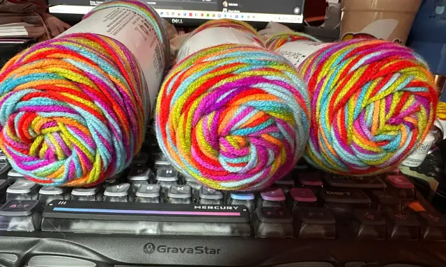 Three balls of brightly colored, variegated yarn sit on a keyboard.