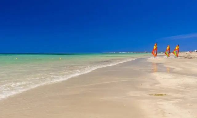 Piękna plaża w Tunezji, idealna na kwiecień. Trzy kolorowe deski windsurfingowe czekają na wiatr.