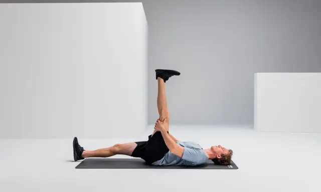 Mann liegt auf Matte, dehnt Bein für Hamstring Training.