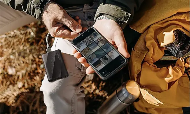 Un homme charge son téléphone avec une batterie externe, une aide précieuse pour comment organiser son téléphone et ses photos en voyage.