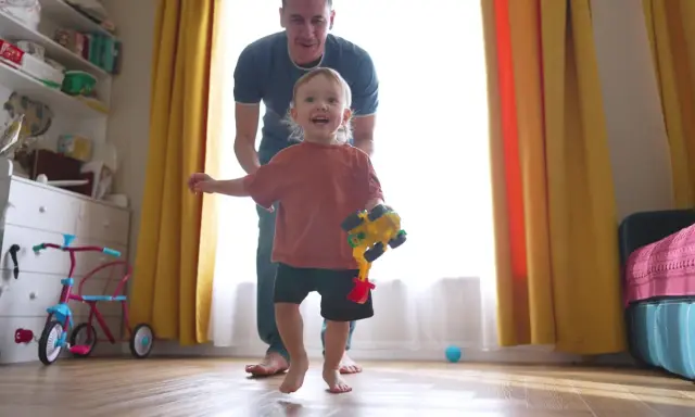 Szczęśliwy 2 latek z zabawką w ręku, prowadzony przez tatę.