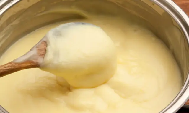 Une cuillère en bois remue une crème pâtissière maison onctueuse dans une casserole.
