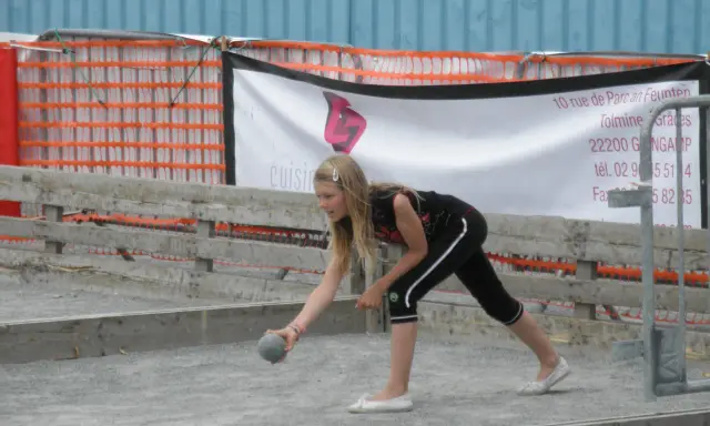 Jeune fille lançant une boule sur un terrain de pétanque, peut-être pour une partie de boule bretonne.