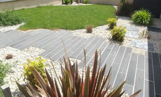 Chemin en dalles grises et gravier blanc, pelouse verte et plantes décoratives. Un jardin facile d'entretien.