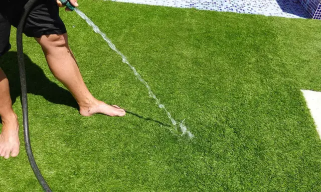 Persona riega césped artificial con manguera. Aprende cómo limpiar césped artificial fácilmente para mantenerlo verde y fresco.
