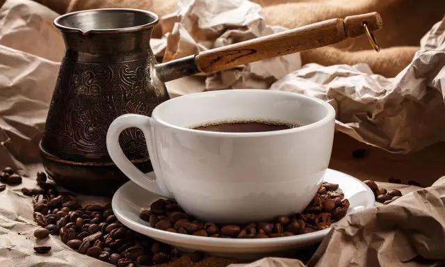 Eine Tasse heißer Espresso Mokka, umgeben von gerösteten Kaffeebohnen und einer traditionellen Mokkakanne.