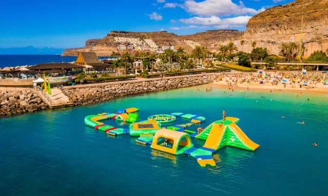 Divertimento acquatico a Gran Canaria con bambini: scivoli gonfiabili e giochi in mare su una spiaggia affollata.