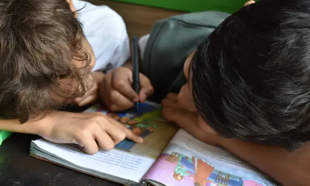 Due bambini studiano insieme, uno scrive mentre l'altro indica il libro. Un esempio di peer learning.
