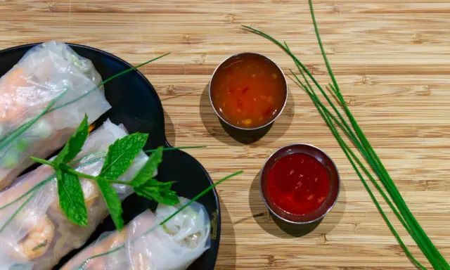 Rouleaux de printemps frais sur une assiette noire, accompagnés de deux sauces : une sauce aigre douce orangée et une sauce rouge.