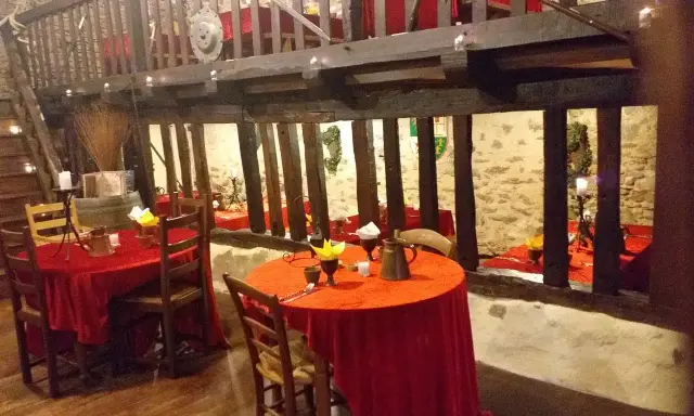 Ambiance d'une auberge moyen âge avec tables dressées de nappes rouges, poutres apparentes et murs en pierre.