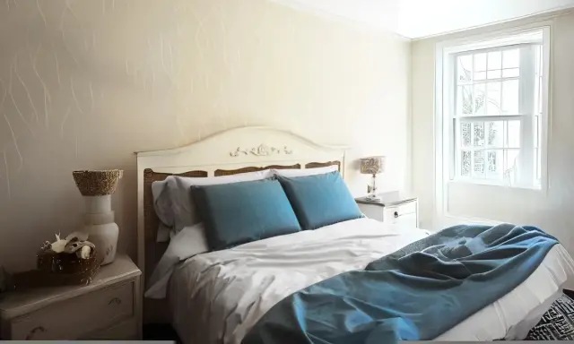 Habitación con cama matrimonial, almohadas azules y manta a juego. Las medidas de camas varían, pero esta parece cómoda.