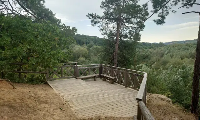 Drewniany taras widokowy z ławką w skalnym mieście Ciężkowice. Widok na zalesione wzgórza.