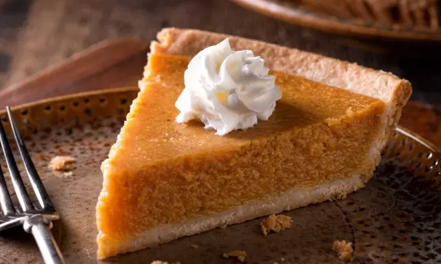 Kawałek pysznego pumpkin pie z bitą śmietaną na talerzu, gotowy do zjedzenia.