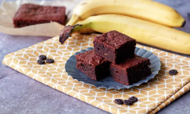 Saftige bananen brownies auf einem gelben Tuch, daneben reife Bananen.