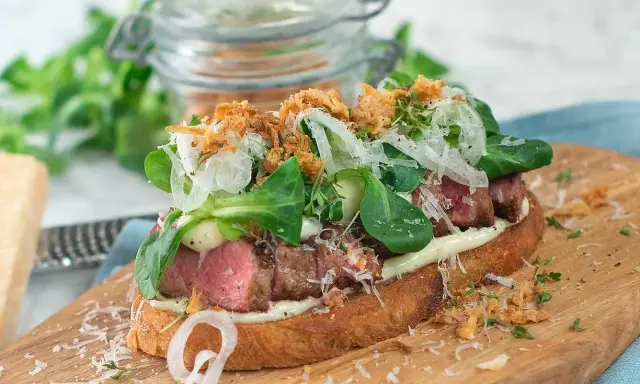 En läcker steak sandwich med saftigt kött, krispig sallad, lök och riven ost på rostat bröd.