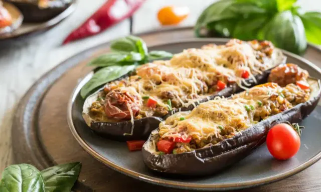 Berenjenas rellenas de atún, gratinadas con queso y decoradas con albahaca y tomate. Un plato delicioso y fácil de preparar.