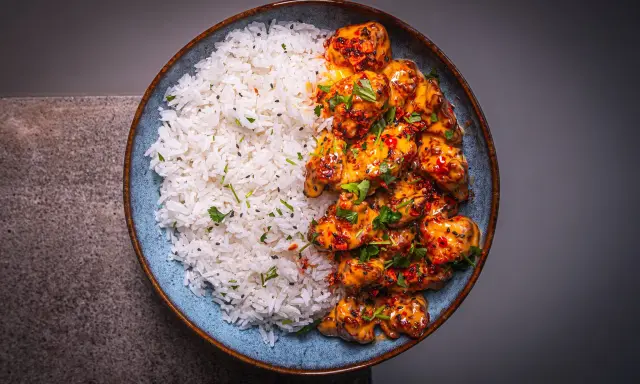 Schüssel mit weißem Reis und würzigem Bang Bang Chicken, garniert mit Koriander und Sesam.