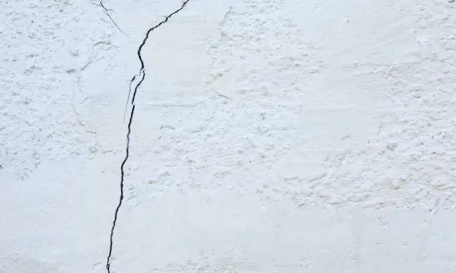 Un muro de casa blanco con una grieta oscura que lo atraviesa. La textura es rugosa y desigual.