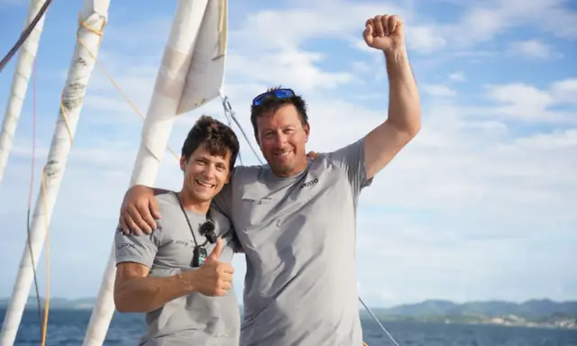 Guillaume Pirouelle et son coéquipier célèbrent une victoire sur l'eau, bras levés et souriants, sous un ciel bleu.