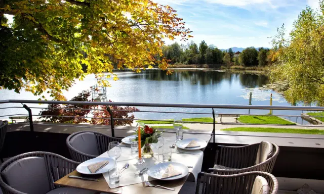 Gedeckter Tisch mit Blick auf einen See und Herbstlaub.