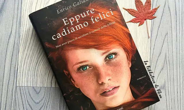 Copertina del libro "Eppure cadiamo felici" di Enrico Galiano, con il volto di una ragazza dai capelli rossi e occhi azzurri. Una foglia d'acero rossa completa la scena.