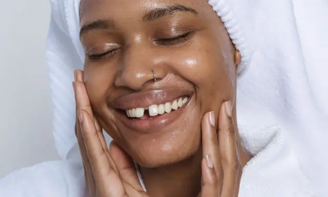 Visage radieux d'une femme souriante, peau hydratée après l'utilisation de rétinol. Elle porte une serviette sur la tête et un peignoir blanc.