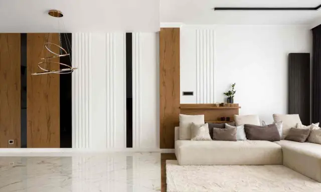 Interni di una casa minimalista con divano beige, tappeto soffice e lampadario moderno. Pareti con pannelli in legno e finiture bianche.