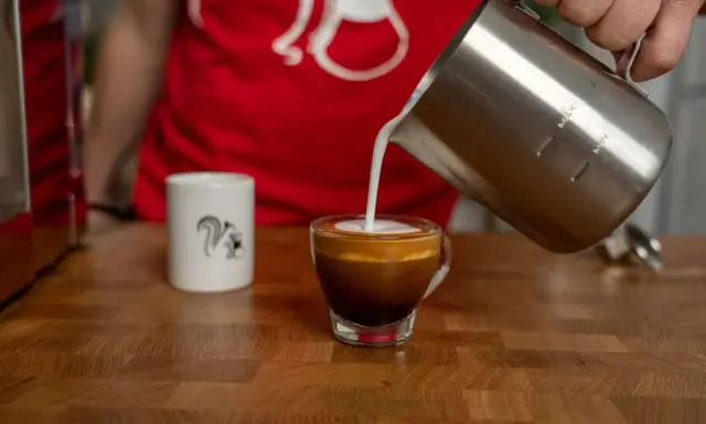 Milchschaum fließt in einen Espresso, um einen perfekten Espresso Macchiato zu kreieren.