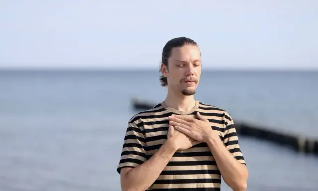 Mann mit geschlossenen Augen und Händen auf der Brust, genießt die frische Meeresluft. Eine asthma kur am meer kann Wunder wirken.
