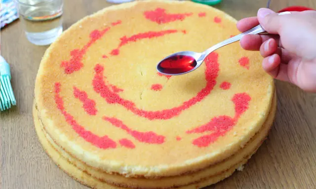 Un cucchiaino di sciroppo rosso viene versato su un pan di spagna decorato con un motivo a spirale. La bagna per pan di spagna renderà la torta più umida e saporita.